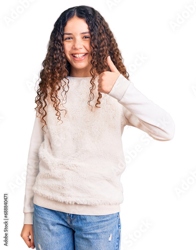 Beautiful kid girl with curly hair wearing casual clothes doing happy thumbs up gesture with hand. approving expression looking at the camera showing success. photo