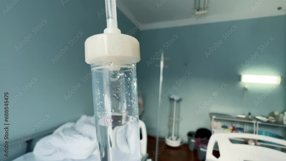 Drip chamber in an IV hanging on a stand against the background of blurred medical beds in a clinic ward Drip chamber in an IV hanging on a stand against the background of blurred medical beds in a clinic ward