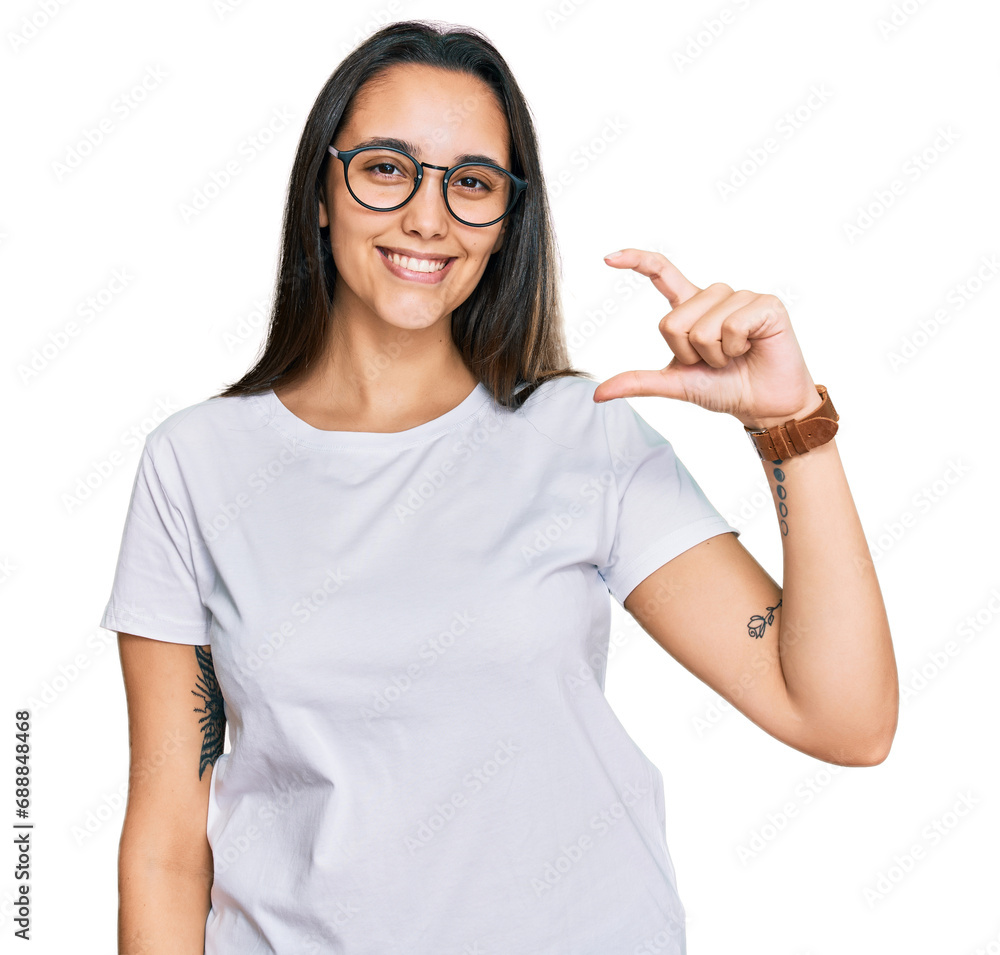 Young hispanic woman wearing casual white t shirt smiling and confident gesturing with hand doing small size sign with fingers looking and the camera. measure concept. Young hispanic woman wearing casual white t shirt smiling and confident gesturing with hand doing small size sign with fingers looking and the camera. measure concept.