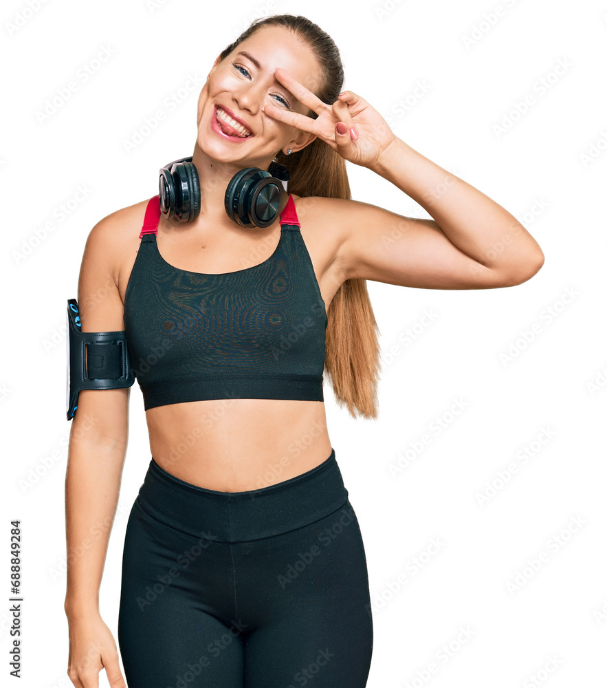 Beautiful blonde woman wearing gym clothes and using headphones doing peace symbol with fingers over face, smiling cheerful showing victory Beautiful blonde woman wearing gym clothes and using headphones doing peace symbol with fingers over face, smiling cheerful showing victory