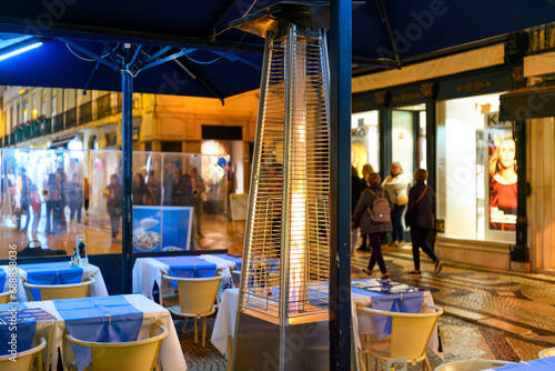 A burning gas flame heater warms tables at a sidewalk cafe at night in the touristic main shopping and dining street of Rua Agusta in Lisbon, Portugal.