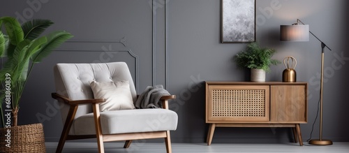 Stylishly decorate living room with chic chair, wooden desk, plants, cube, lamp, mock up poster frame, macrame, and elegant accessories. Gray walls.