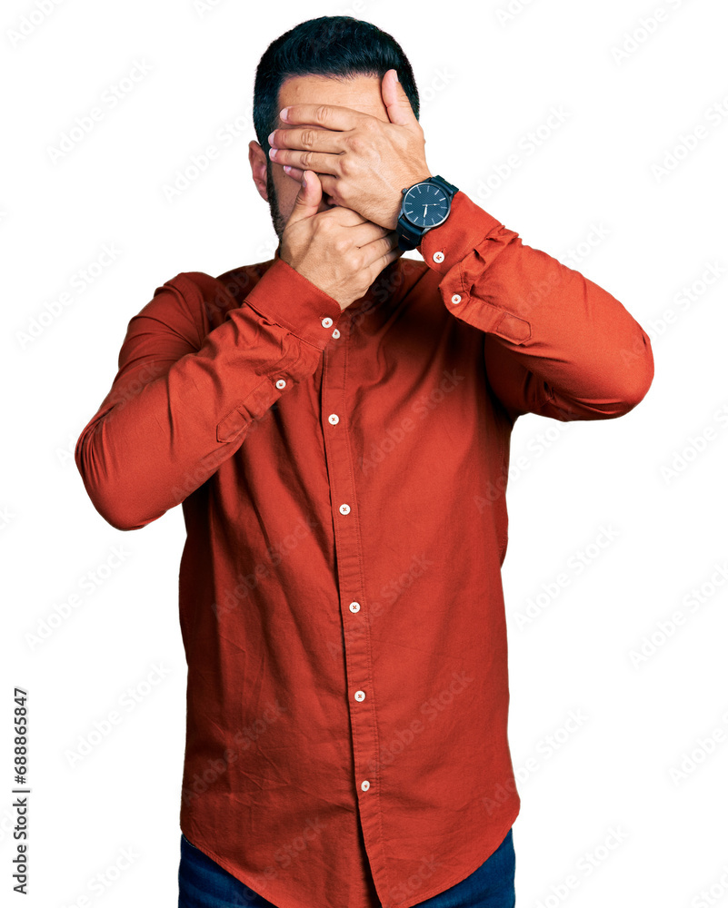 Young hispanic man with beard wearing casual shirt covering eyes and mouth with hands, surprised and shocked. hiding emotion Young hispanic man with beard wearing casual shirt covering eyes and mouth with hands, surprised and shocked. hiding emotion