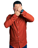 Young hispanic man with beard wearing casual shirt covering eyes and mouth with hands, surprised and shocked. hiding emotion