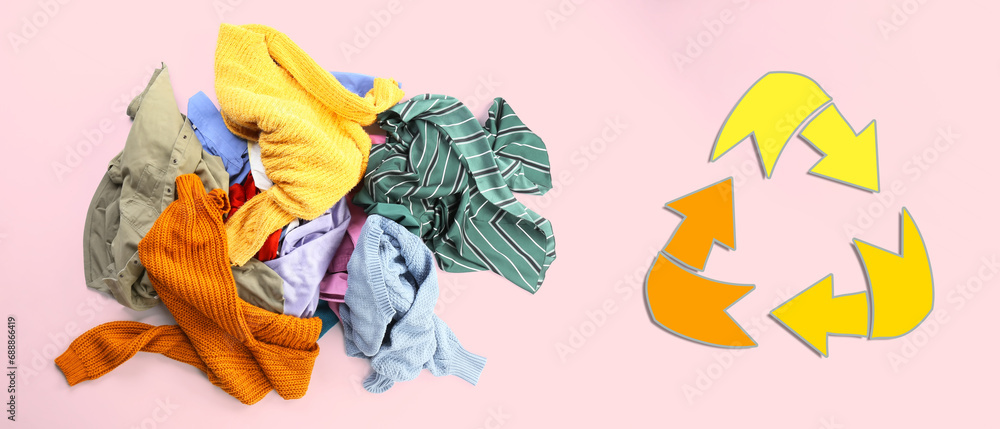 Heap of clothes and recycling symbol on pink background. Ecology concept