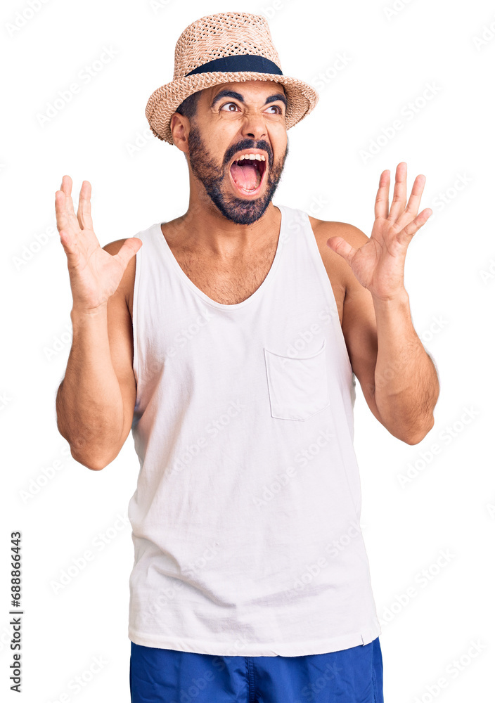 Young hispanic man wearing casual summer hat crazy and mad shouting and yelling with aggressive expression and arms raised. frustration concept. Young hispanic man wearing casual summer hat crazy and mad shouting and yelling with aggressive expression and arms raised. frustration concept.