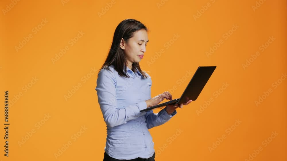 Casual person navigating online on laptop in studio, looking for inspiration on wireless pc against orange background. Asian woman browsing webpages on internet, search project. Casual person navigating online on laptop in studio, looking for inspiration on wireless pc against orange background. Asian woman browsing webpages on internet, search project.