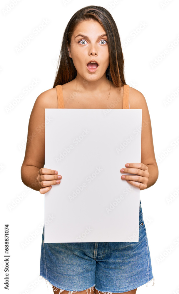 Young caucasian woman holding blank empty banner scared and amazed with open mouth for surprise, disbelief face Young caucasian woman holding blank empty banner scared and amazed with open mouth for surprise, disbelief face