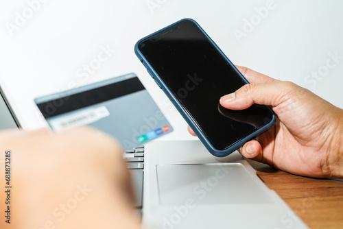 Close up male hand holding a bank credit card doing online transactions using a laptop and smart phone