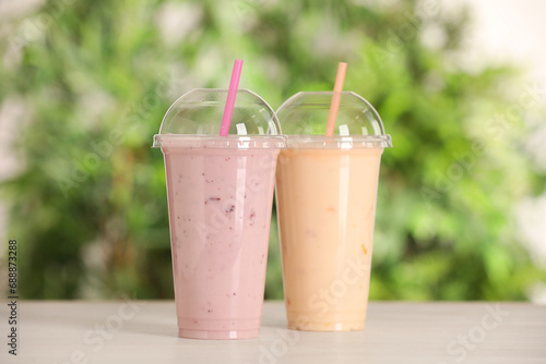 Plastic cups with different tasty smoothies on wooden table outdoors