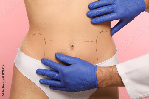 Doctor checking patient's body before cosmetic surgery operation on pink background, closeup