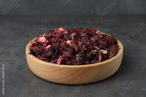 Hibiscus tea. Wooden bowl with dried roselle calyces on grey table, closeup photo