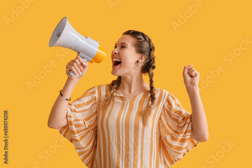 Young woman shouting into megaphone on yellow background