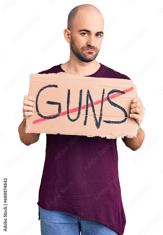 Young handsome man holding prohibited guns banner thinking attitude and sober expression looking self confident Young handsome man holding prohibited guns banner thinking attitude and sober expression looking self confident