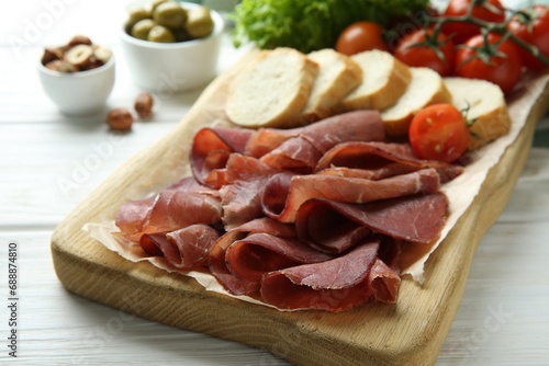 Board with delicious bresaola on white wooden table, closeup