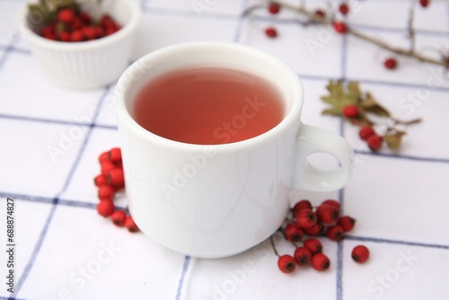 Cup with hawthorn tea and berries on table, closeup