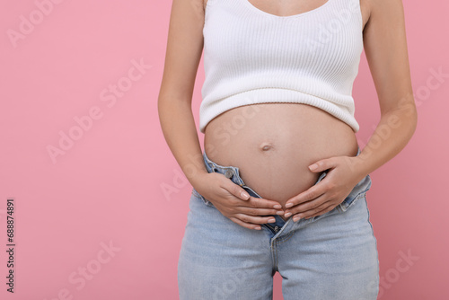 Pregnant woman in jeans on pink background, closeup. Space for text