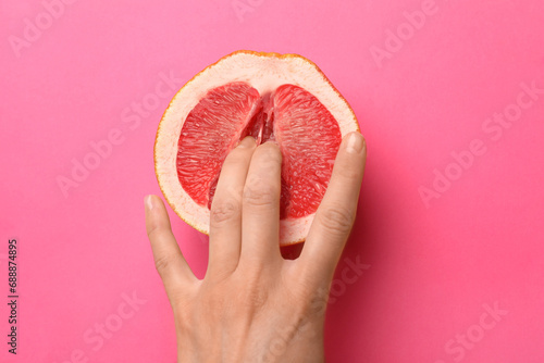 Woman touching half of grapefruit on pink background, top view. Sex concept photo