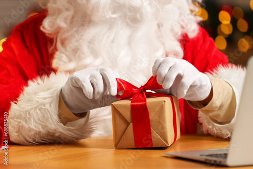 Santa Claus decorating Christmas gift with ribbon at home, closeup
