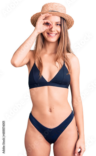 Young beautiful girl wearing bikini and hat doing ok gesture with hand smiling, eye looking through fingers with happy face.