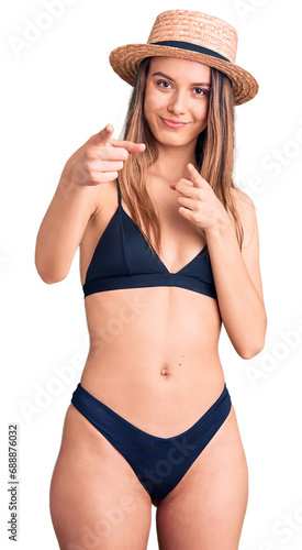 Young beautiful girl wearing bikini and hat pointing fingers to camera with happy and funny face. good energy and vibes.