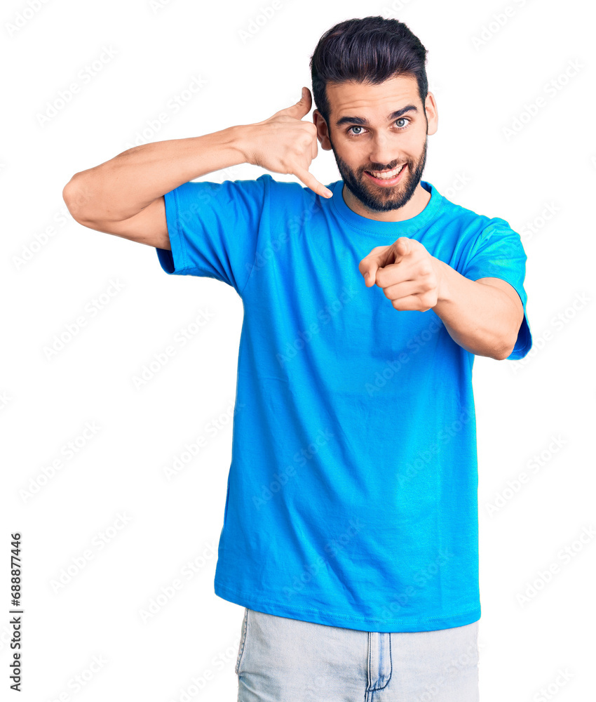 Young handsome man with beard wearing casual t-shirt smiling doing talking on the telephone gesture and pointing to you. call me. Young handsome man with beard wearing casual t-shirt smiling doing talking on the telephone gesture and pointing to you. call me.