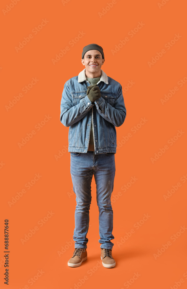 Frozen young man in winter clothes on orange background Frozen young man in winter clothes on orange background