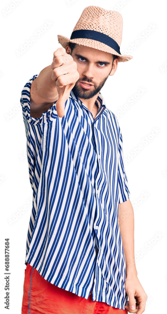 Young handsome man with beard wearing summer hat and striped shirt looking unhappy and angry showing rejection and negative with thumbs down gesture. bad expression. Young handsome man with beard wearing summer hat and striped shirt looking unhappy and angry showing rejection and negative with thumbs down gesture. bad expression.