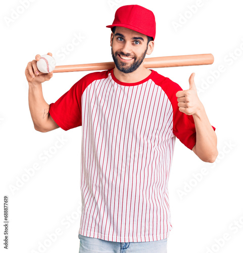 Young handsome man with beard playing baseball holding bat and ball smiling happy and positive, thumb up doing excellent and approval sign