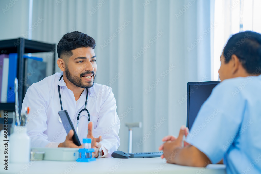 Muslim male and female doctors in medical uniforms was sitting at the patient's examination table and was examining and talking about the patient with a smiling and worried face in hospital. Muslim male and female doctors in medical uniforms was sitting at the patient's examination table and was examining and talking about the patient with a smiling and worried face in hospital.