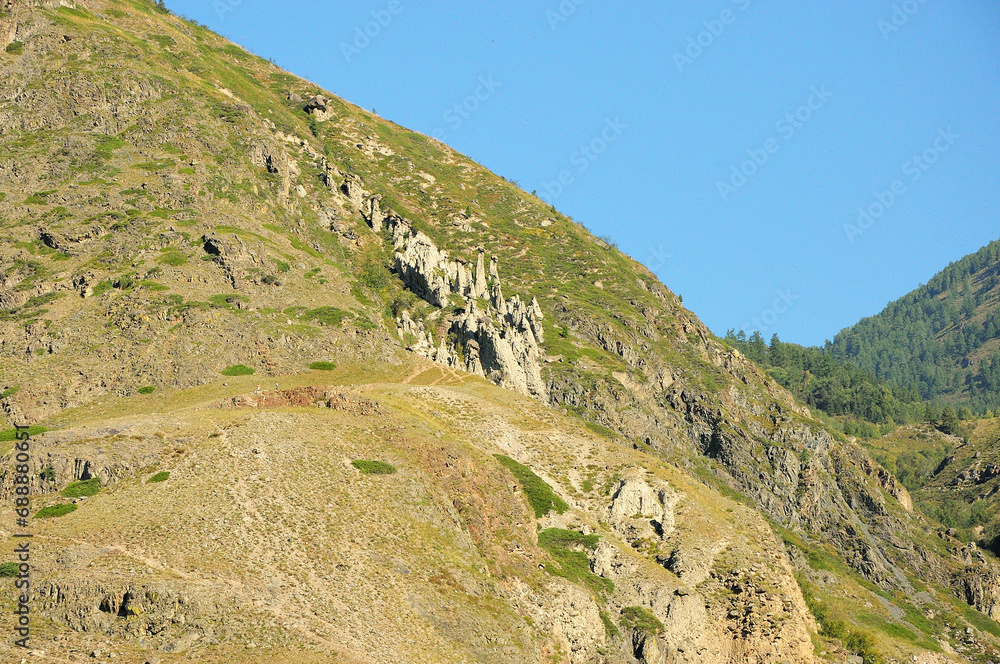 The slope of a high mountain overgrown with grass and unusual stone formations of white sandstone on a steep slope.