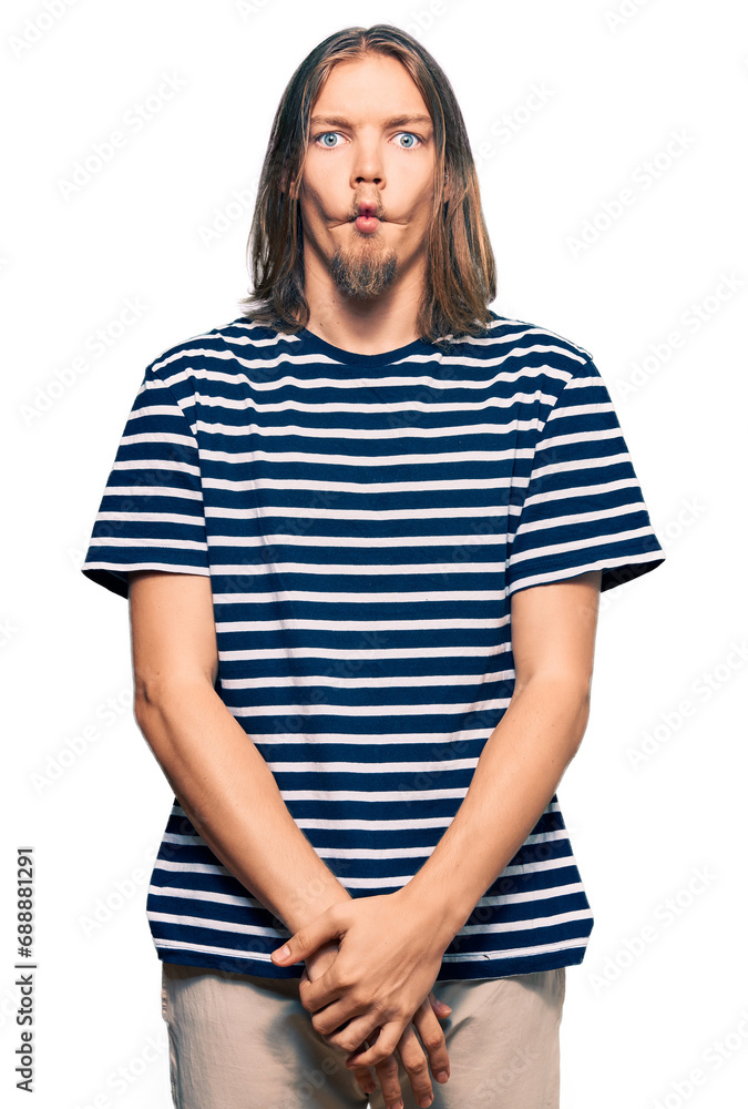 Handsome caucasian man with long hair wearing casual striped t-shirt making fish face with lips, crazy and comical gesture. funny expression. Handsome caucasian man with long hair wearing casual striped t-shirt making fish face with lips, crazy and comical gesture. funny expression.