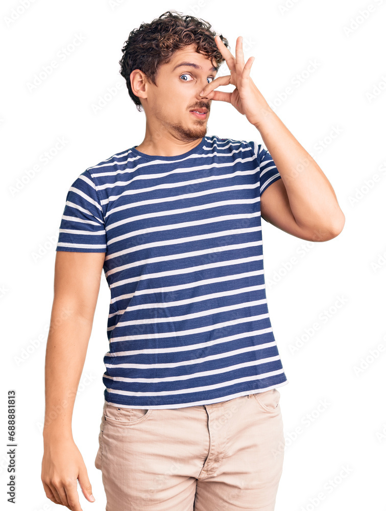 Young handsome man with curly hair wearing casual clothes smelling something stinky and disgusting, intolerable smell, holding breath with fingers on nose. bad smell Young handsome man with curly hair wearing casual clothes smelling something stinky and disgusting, intolerable smell, holding breath with fingers on nose. bad smell
