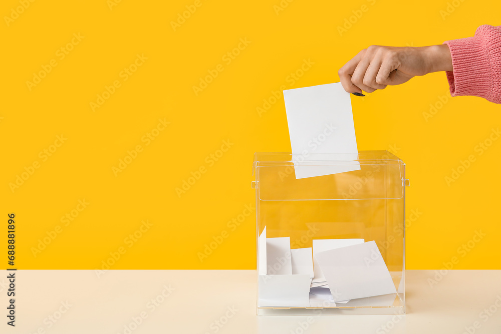 Hand putting voting paper in ballot box on yellow background - obrazy, fototapety, plakaty 