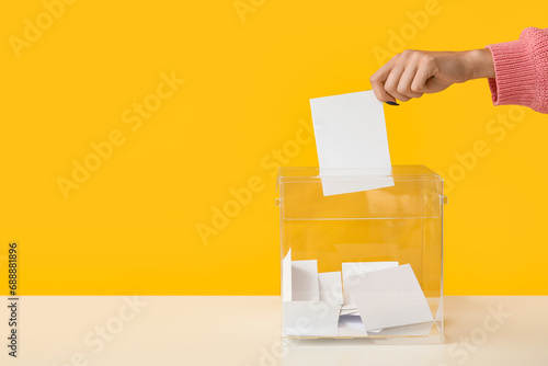 Hand putting voting paper in ballot box on yellow background photo