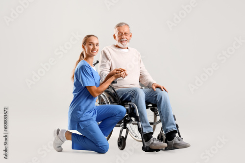 Senior man in wheelchair with nurse on light background