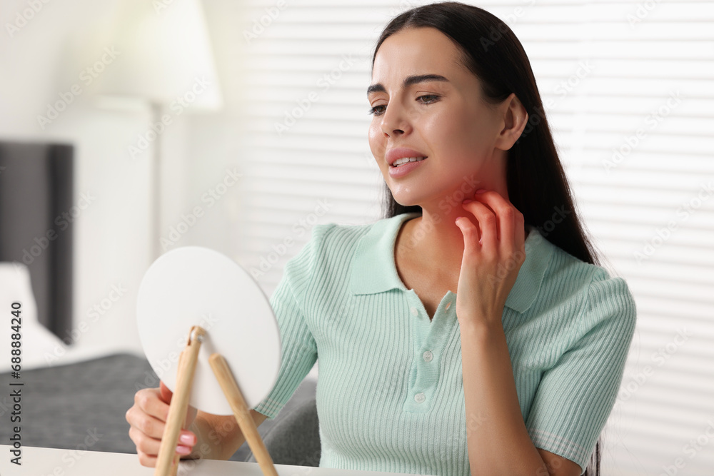 Suffering from allergy. Young woman looking in mirror and scratching her neck at white table indoors Suffering from allergy. Young woman looking in mirror and scratching her neck at white table indoors