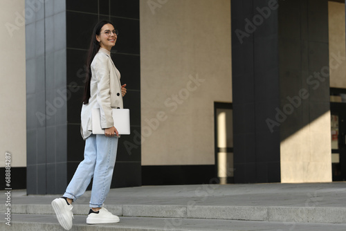 Happy young woman holding modern laptop outdoors. Space for text
