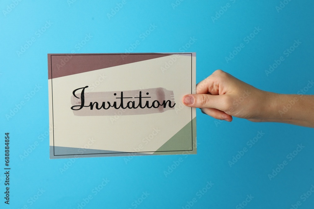 Woman holding beautiful card with word Invitation on light blue background, closeup Woman holding beautiful card with word Invitation on light blue background, closeup