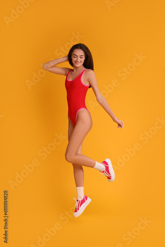 Young woman in stylish swimsuit on yellow background