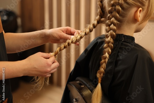Professional hairdresser braiding girl's hair in beauty salon, closeup photo