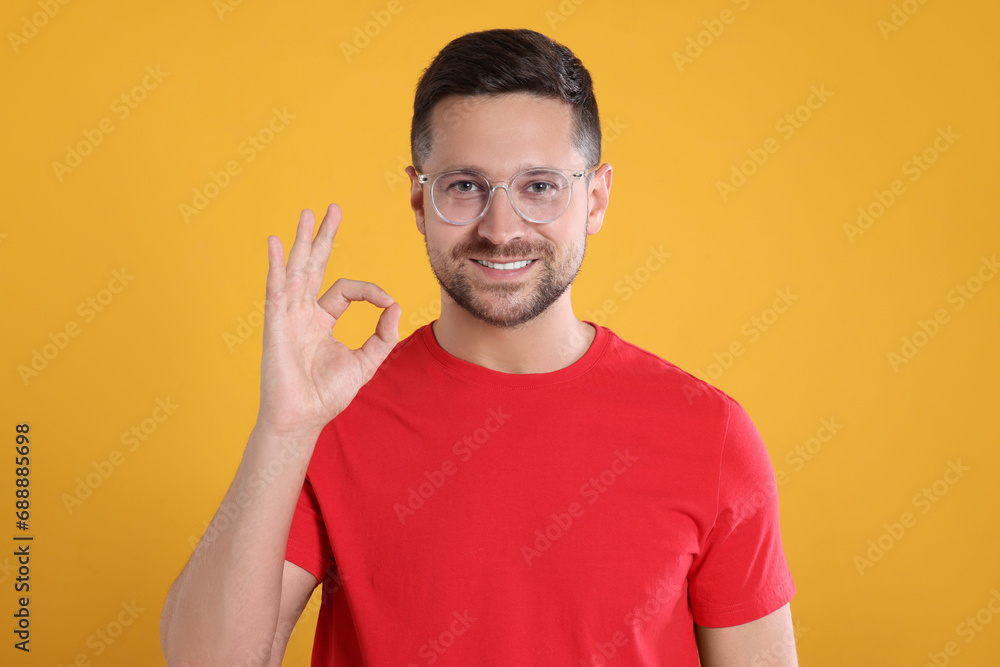 Portrait of happy man in stylish glasses showing ok gesture on yellow background Portrait of happy man in stylish glasses showing ok gesture on yellow background