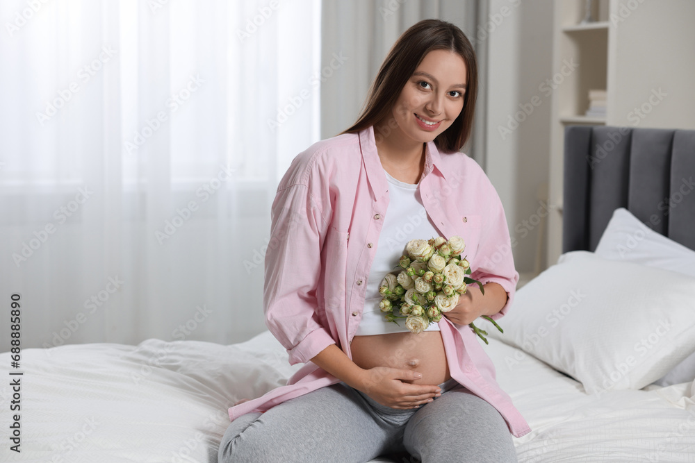 Beautiful pregnant woman with bouquet of roses in bedroom