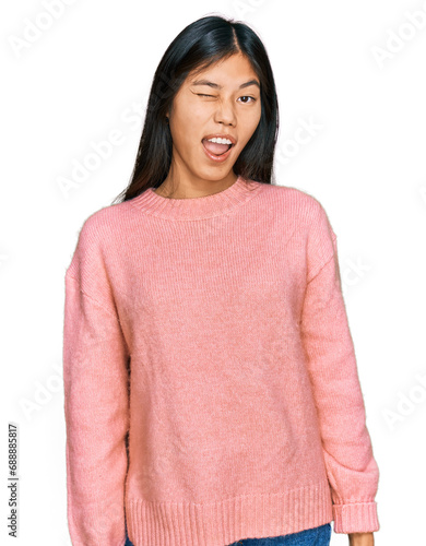 Beautiful young asian woman wearing casual winter sweater winking looking at the camera with sexy expression, cheerful and happy face.