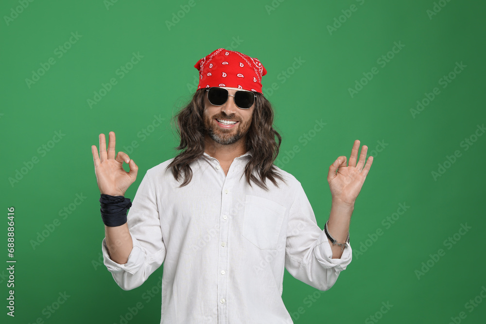 Stylish hippie man in sunglasses showing OK gesture on green background Stylish hippie man in sunglasses showing OK gesture on green background