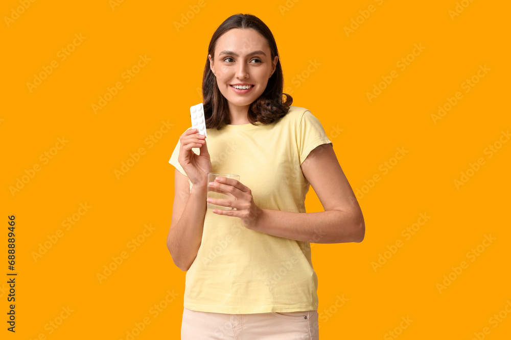 Beautiful young woman with pills and glass of water on yellow background