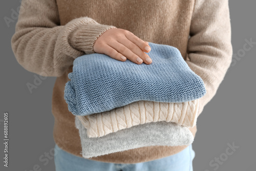Woman holding stack of different stylish sweaters on grey background, closeup photo