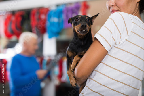 Portrait of happy positive woman visiting pet supplies store with her dog doberman pinscher