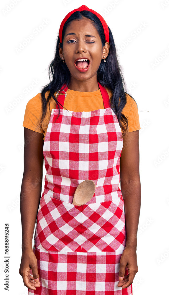 Young indian girl wearing professional baker apron winking looking at the camera with sexy expression, cheerful and happy face. Young indian girl wearing professional baker apron winking looking at the camera with sexy expression, cheerful and happy face.
