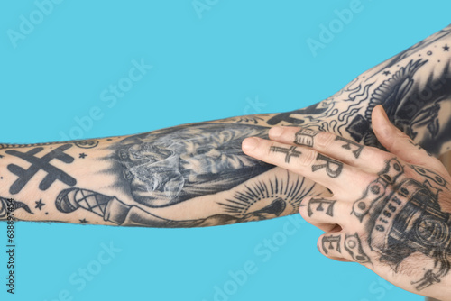 Man applying cream on his arm with tattoos against blue background, closeup photo